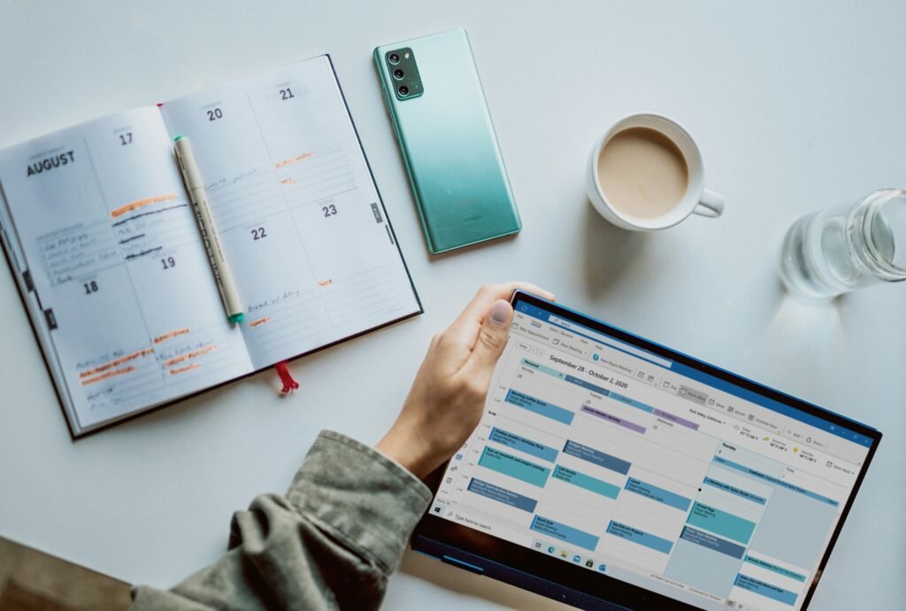 Student writing in a weekly planner beside open textbooks and a laptop