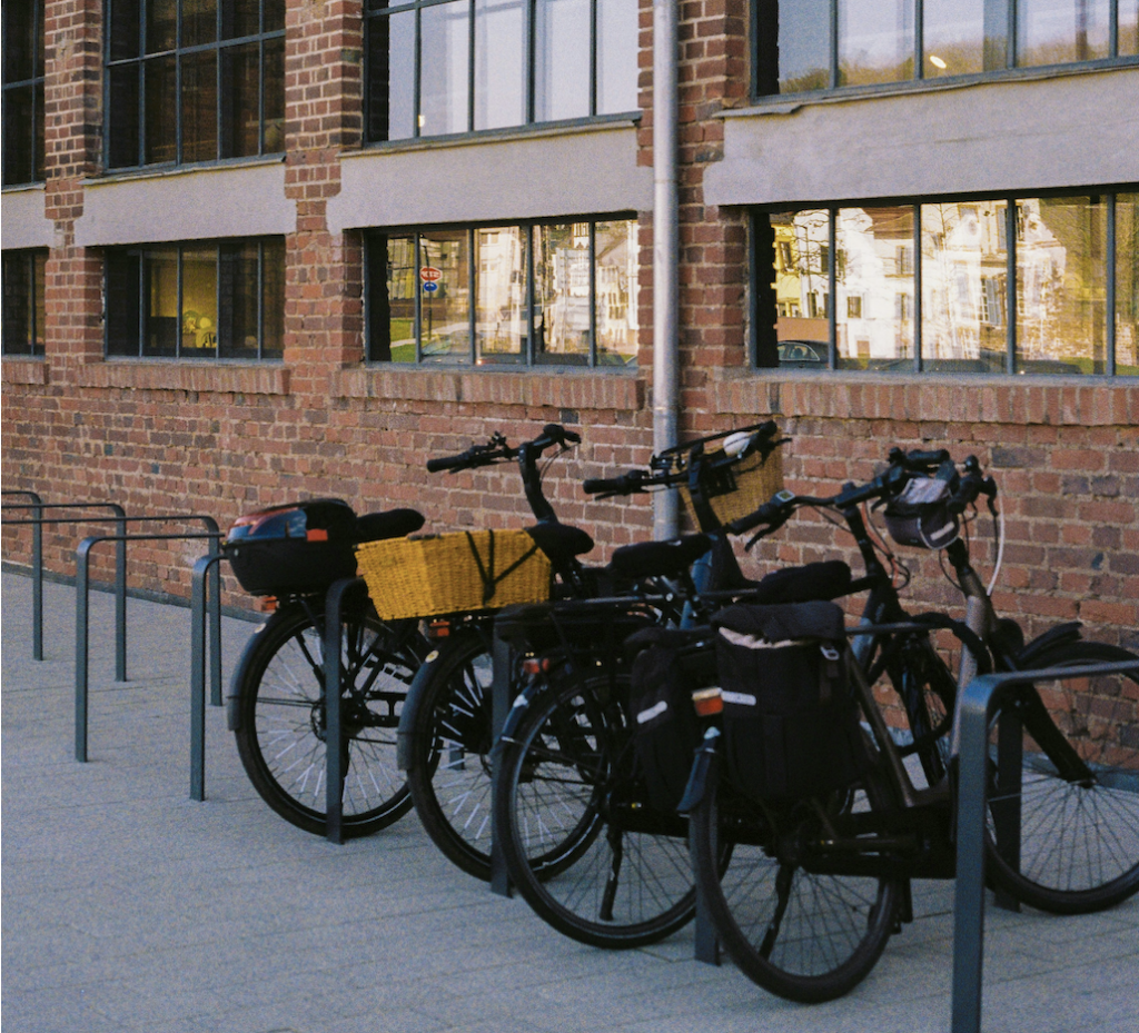 Three bikes leaning against a bike rack next to a brick building at dusk