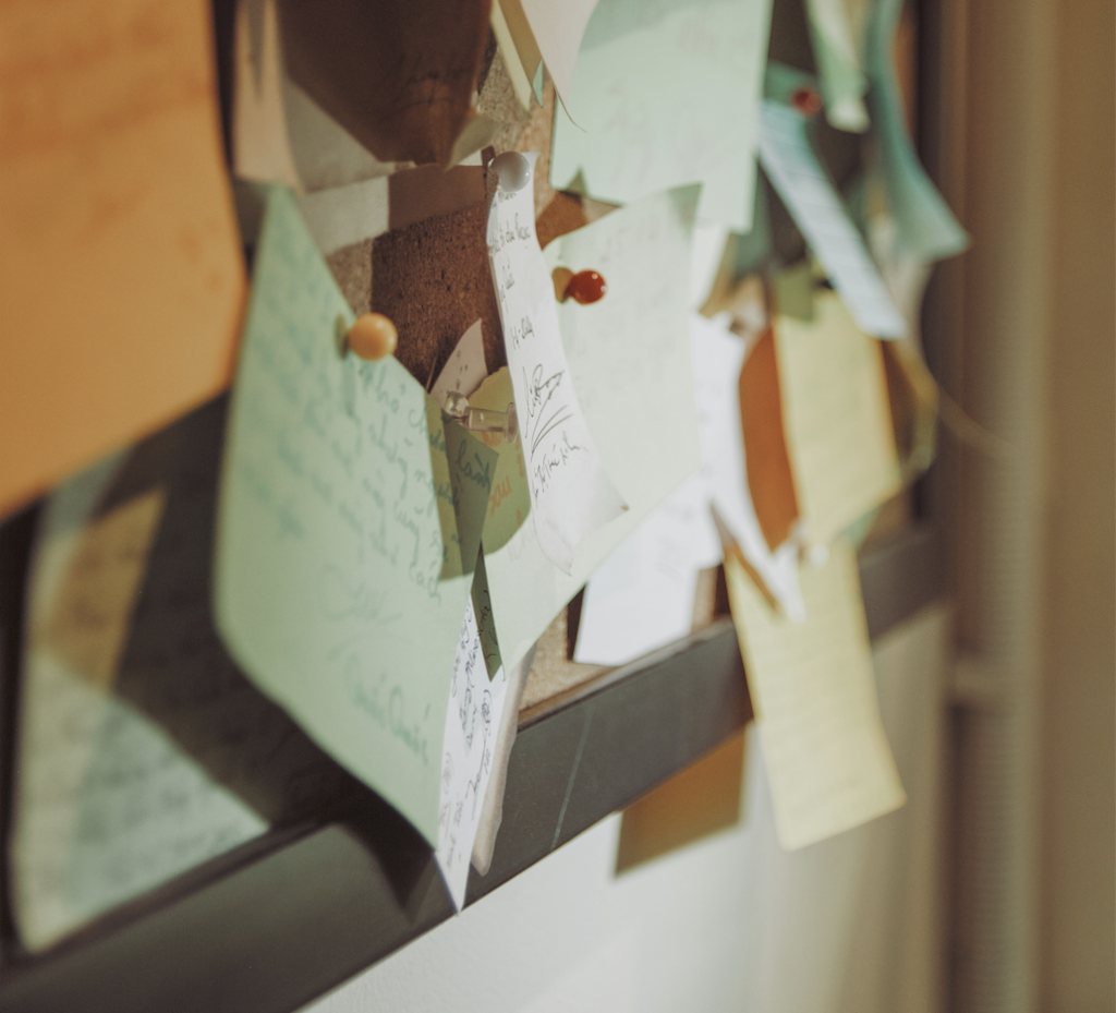 Cropped hand holding a printed page beside a bulletin board of pinned notices